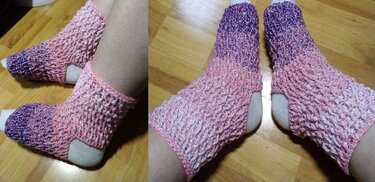 Nahaufnahme handgehäkelter fersenloser Socken in Lila und Rosa auf Holzboden.