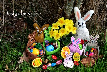 Gestickte Osterhasen und Körbchen mit bunten Eiern und gelben Frühlingsblumen auf Gras