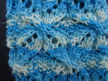 Nahaufnahme eines blau-weißen Strickmusters mit Loch- und Zopfmaschen