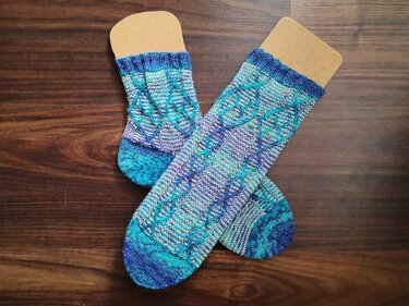 Paar handgestrickter Zopfsocken in Blau und Türkis mit Zopfmuster auf Holz