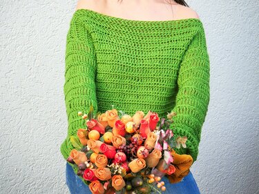 Gehäkelter grüner Off-Shoulder-Pullover mit sichtbarem Maschenmuster und Blumenstrauß
