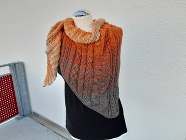 Mannequin trägt gestricktes Dreieckstuch mit Farbverlauf von Beige über Orange zu Grau und Zopfmuster