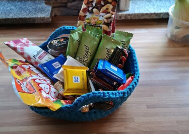 Gehäkelter türkisfarbener Korb gefüllt mit Schokoriegeln und Bonbons auf einer Holzarbeitsplatte