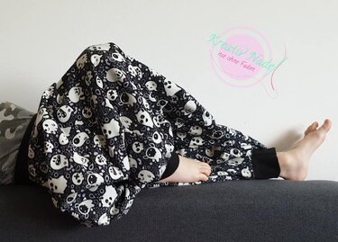 Kind liegt auf Sofa und trägt lockere schwarz-weiße Hose mit Totenkopf-Muster und elastischen Knöchelbündchen, barfuß