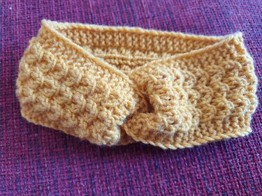 Gestricktes senfgelbes Baby-Stirnband mit Knoten auf violettem Stoff