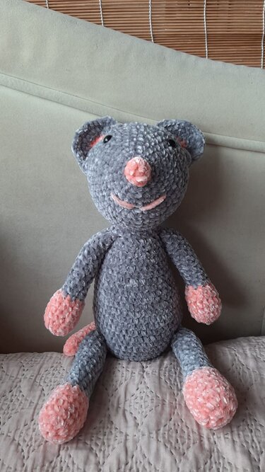 Gehäkelte graue Amigurumi-Maus mit rosa Nase, Pfoten und Schwanz, sitzend