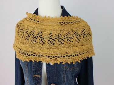 Senfgelber gestrickter Loop mit Zopf- und Lochmuster auf einer Schneiderpuppe