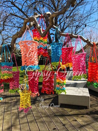 Bunte gehäkelte Laternen und Hängedekorationen an den Ästen eines Baumes über einer Holzterrasse.