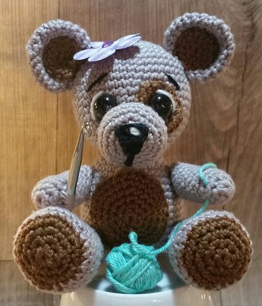 Nahaufnahme eines gehäkelten Amigurumi-Teddys mit Häkelnadel und türkisfarbenem Garn