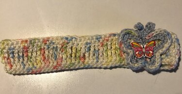 Gehäkeltes Baby-Stirnband in Pastell mit hellblauer Blüten-Applikation und buntem Schmetterlingsknopf