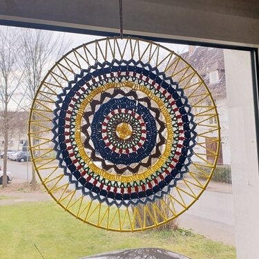 Rundes gehäkeltes Mandala in Gelb, Dunkelblau, Rot und Braun, aufgehängt im Fenster