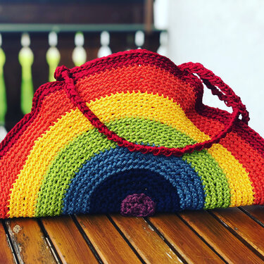 Gehäkelte Tasche im Halbkreis-Regenbogenmuster mit rotem Träger auf Holzuntergrund