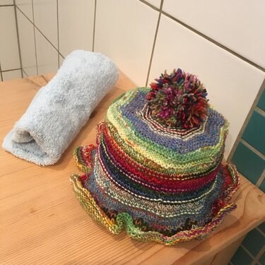 Mehrfarbige gestrickte Mütze mit Bommel auf Holzablage neben Handtuch