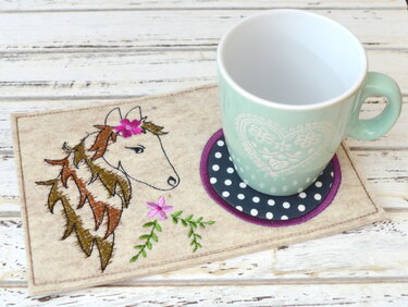 Gestickter Filz-Tassenteppich mit stilisiertem Pferdekopf, Blumenstickerei und rundem gepunktetem Untersetzer unter einer mintgrünen Tasse