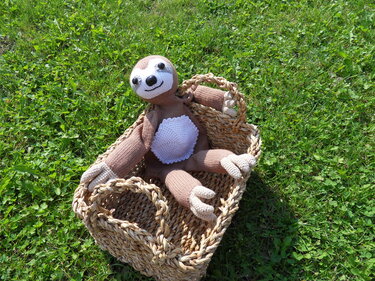 Handgestricktes Faultier-Stofftier in Weidenkorb auf grüner Wiese