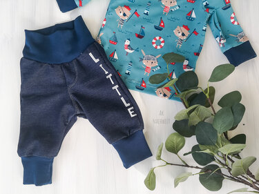 Babykleidungs-Set: dunkelblaue Hose mit LITTLE-Schriftzug und hellblaues Shirt mit maritimen Tiermotiven neben grünen Zweigen.