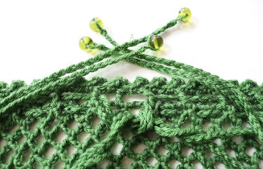 Nahaufnahme eines grünen Häkelnetzes mit offenem Maschenmuster und gelb-grünen Perlen an der oberen Kordel.