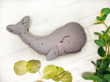 Gehäkelter grauer Wal-Amigurumi liegend mit gesticktem Gesicht und angenähter Flosse