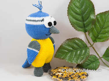 Gehäkelter Amigurumi-Vogel blau gelb mit grauem Schnabel neben Futterschale