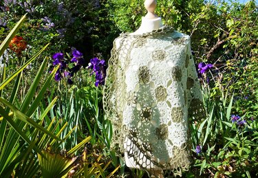 Schaufensterpuppe trägt gehäkeltes Rechtecktuch aus creme- und olivfarbenen Granny-Motiven mit Spitzenrand, im Gartenhintergrund