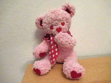 Rosa flauschiger Häkel-Teddybär mit roten Herzen an Pfoten, Nase und Augen sowie einem Herzchen-Halstuch
