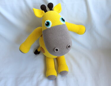 Gelbe gehäkelte Amigurumi-Giraffe mit grauem Maul und türkisfarbenen Augen auf hellem Hintergrund
