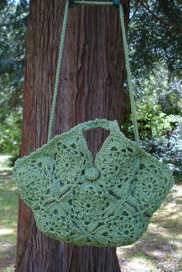 Light green crocheted bag with granny-square motifs hanging on a tree.