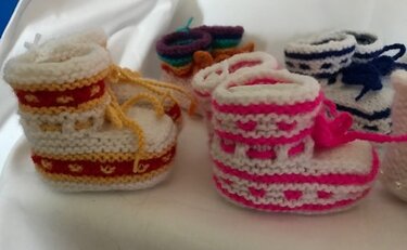 Nahaufnahme gestrickter Babyschuhe mit sichtbarer Maschenstruktur, Schnürbändern und bunten Zierkanten