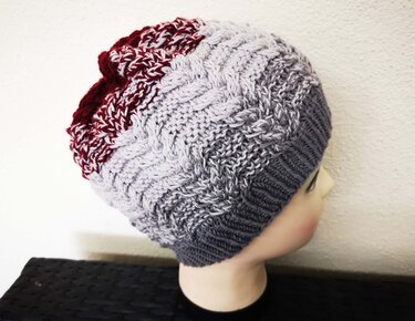 Gestrickte Damenmütze mit Zopfmuster in Grau und Weinrot auf einer Schaufensterpuppe