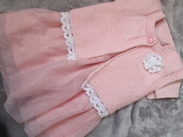 Gestrickte rosa Babyweste mit Häkelblüte über rosa Tüllrock