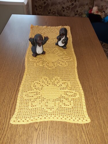 Gelber gehäkelter Tischläufer mit Spitzenmuster auf Holztisch, zwei Maulwurffiguren als Deko