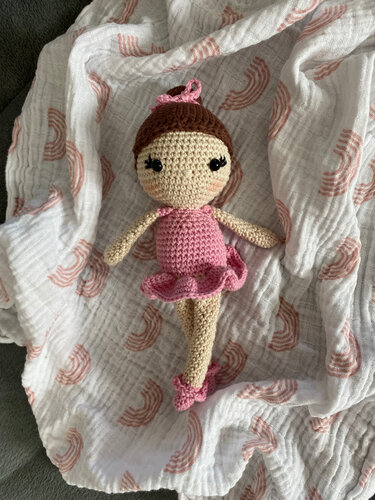 Gehäkelte Ballerina-Amigurumi mit rosa Kleid, Rüschenrock und braunem Dutt auf weißer Decke mit Regenbogenmuster