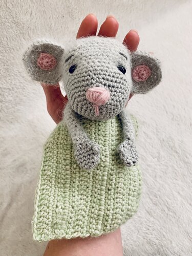 Gehäkelte graue Maus-Handpuppe mit rosa Ohren und Nase und hellgrünem Körper, von einer Hand gehalten vor hellem Hintergrund.