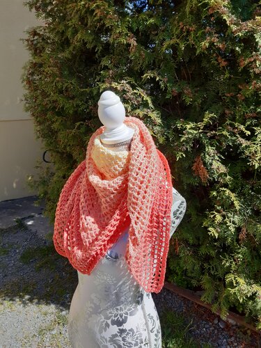 Gehäkelter Schal in Koralle und Creme auf Schaufensterpuppe vor grüner Hecke