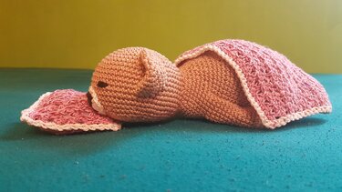 Gehäkeltes braunes Amigurumi-Schlafbärchen unter rosa Decke