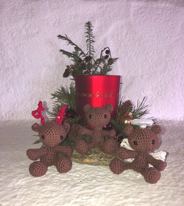 Drei braune gehäkelte Amigurumi-Bären (Rentier, Engel, klassischer Bär) vor rotem Kerzenhalter und Tannengrün
