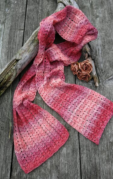 Rosa-roter Strickschal mit Ajourmuster auf rustikalem Holz, seitlich drapiert