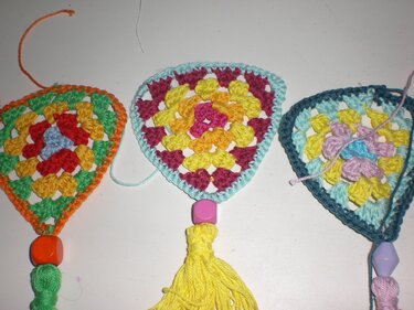 Drei gehäkelte, dreieckige Fächermotive im Granny‑Stil mit Perlen und Quasten auf hellem Hintergrund.