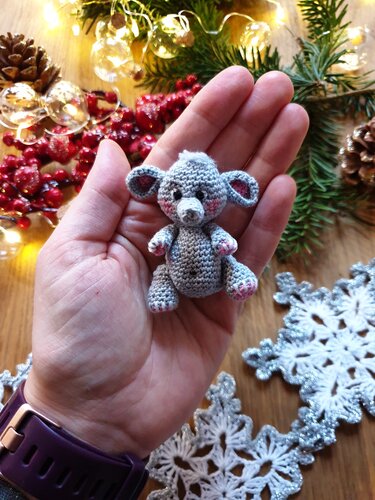 Hand hält einen kleinen grauen Amigurumi-Elefanten mit rosa Akzenten vor weihnachtlicher Dekoration