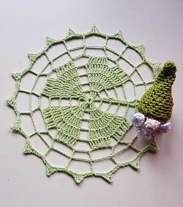 Light green circular crocheted doily with spiky edge and a small crocheted gnome with a green hat.