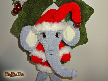 Gehäkelter grauer Elefant in rotem Weihnachtskostüm vor grünem gehäkeltem Kranz mit roten Kugeln