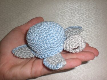 Hellblau-graue gehäkelte Schildkröte in einer Hand.