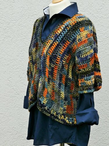 Gehäkelter Damen-Poncho in Orange, Blau und Grün mit V-Ausschnitt auf einer Schaufensterpuppe über einem dunkelblauen Hemd.