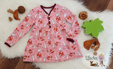 Rosa Kinderkleid mit Fuchs- und Hasenmuster auf weißem, flauschigem Untergrund