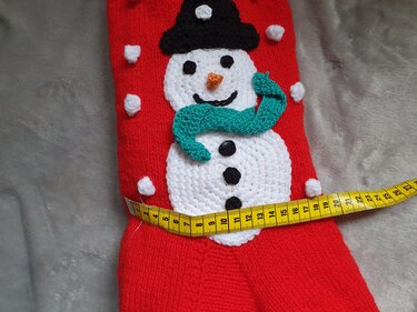 Roter gestrickter Weihnachtsstiefel mit aufgenähtem Schneemann und gelbem Maßband