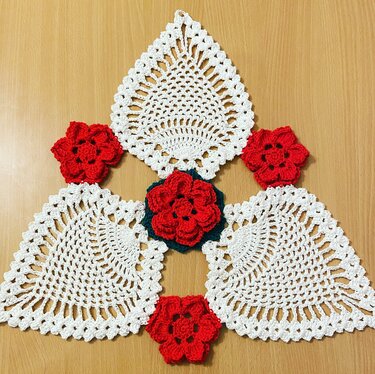 Weiße gehäkelte Deckchen und rote Häkelblumen auf Holzoberfläche