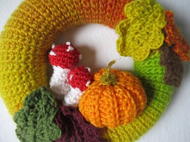 Gehäkelter Herbst-Türkranz mit orangem Kürbis, roten Pilzen mit weißen Punkten und mehrfarbigen Blattapplikationen auf einem gelb-grünen Ring