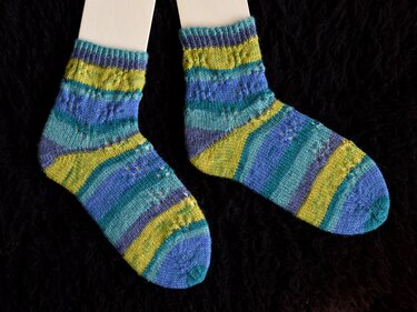 Paar gestrickter Socken in Blau-, Türkis- und Gelbgrün-Streifen mit Lochmuster auf dunklem Hintergrund.