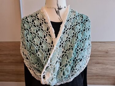 Gehäkelter Loopschal in Mint und Weiß mit Muschelmuster auf einer Büste.