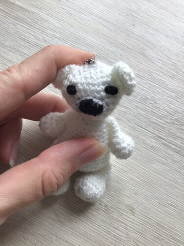 Hand hält kleinen weißen gehäkelten Amigurumi-Bären mit Metallöse